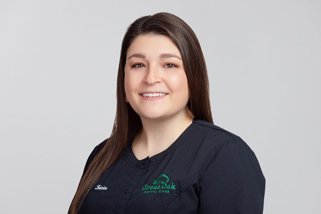 Headshot of smiling female dental hygienist wearing logo polo shirt against a grey background. 