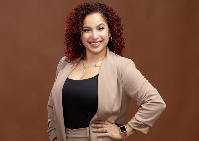 Professional photo of a smiling business woman with pink and black hair with a textured brown headshot background.