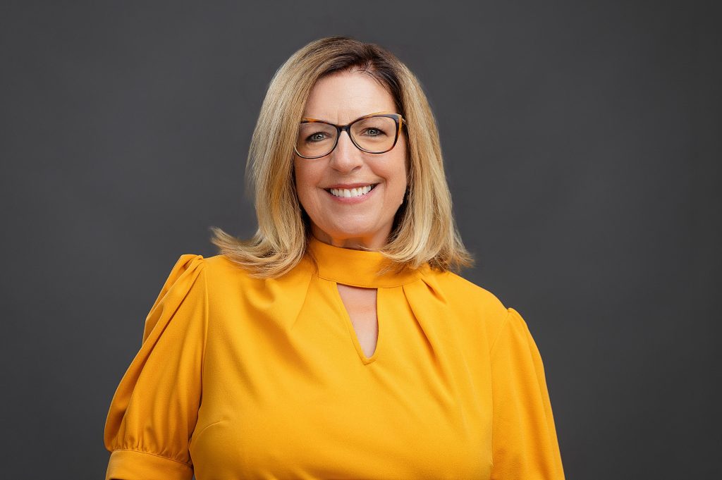 Real estate agent professional headshot of a smiling woman wearing yellow against a modern grey background