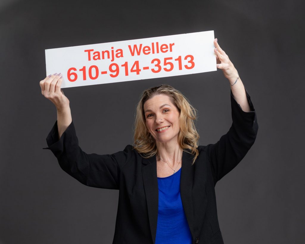 Smiling real estate agent holds up a sign with her name and phone number on