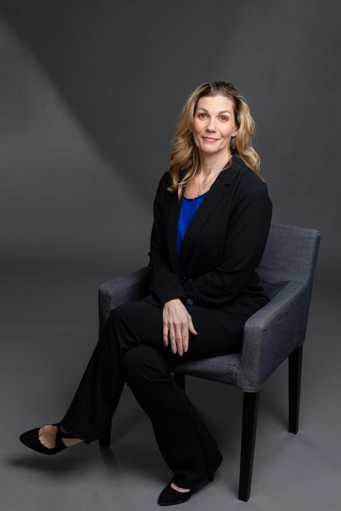 Headshot of businesswoman sitting in a chair. She's wearing a black suit. 