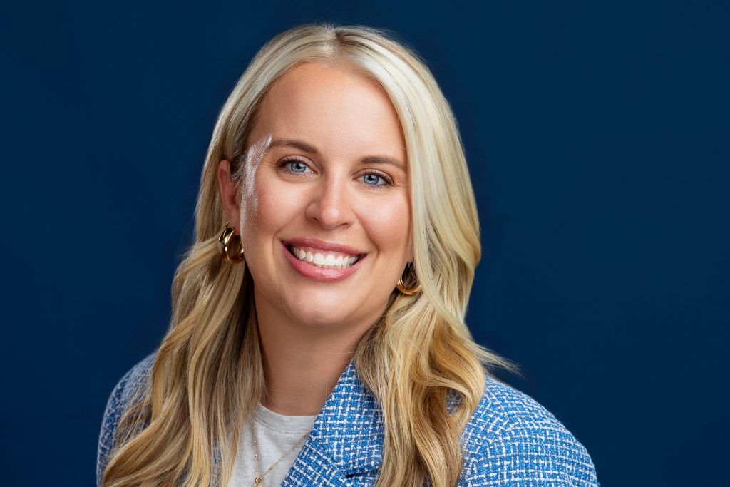 Close up headshot of real estate agent with a blue blazer on a navy background. 