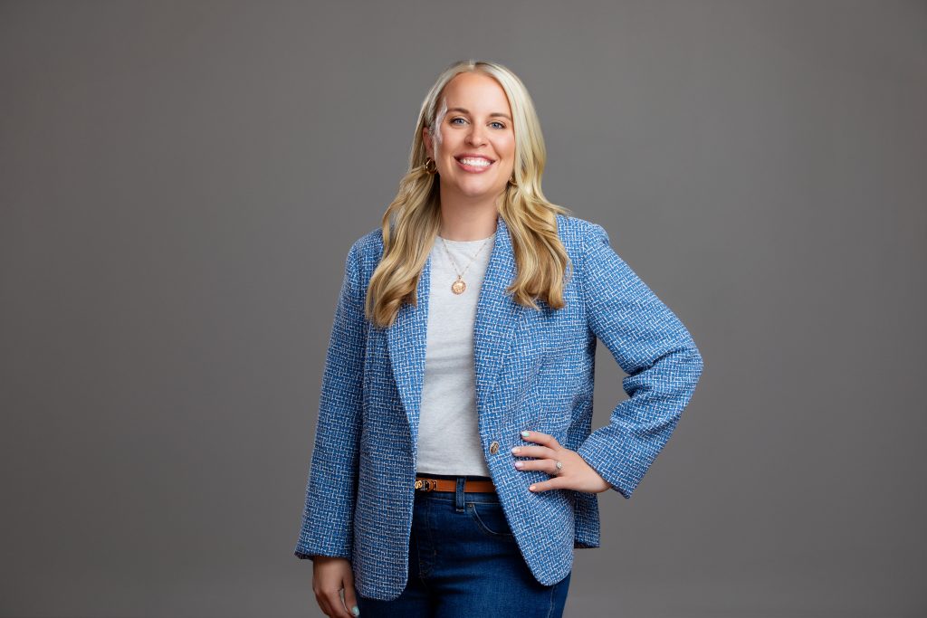 Zoomed out photo of a real estate agent standing with her hand on her hip and smiling. 