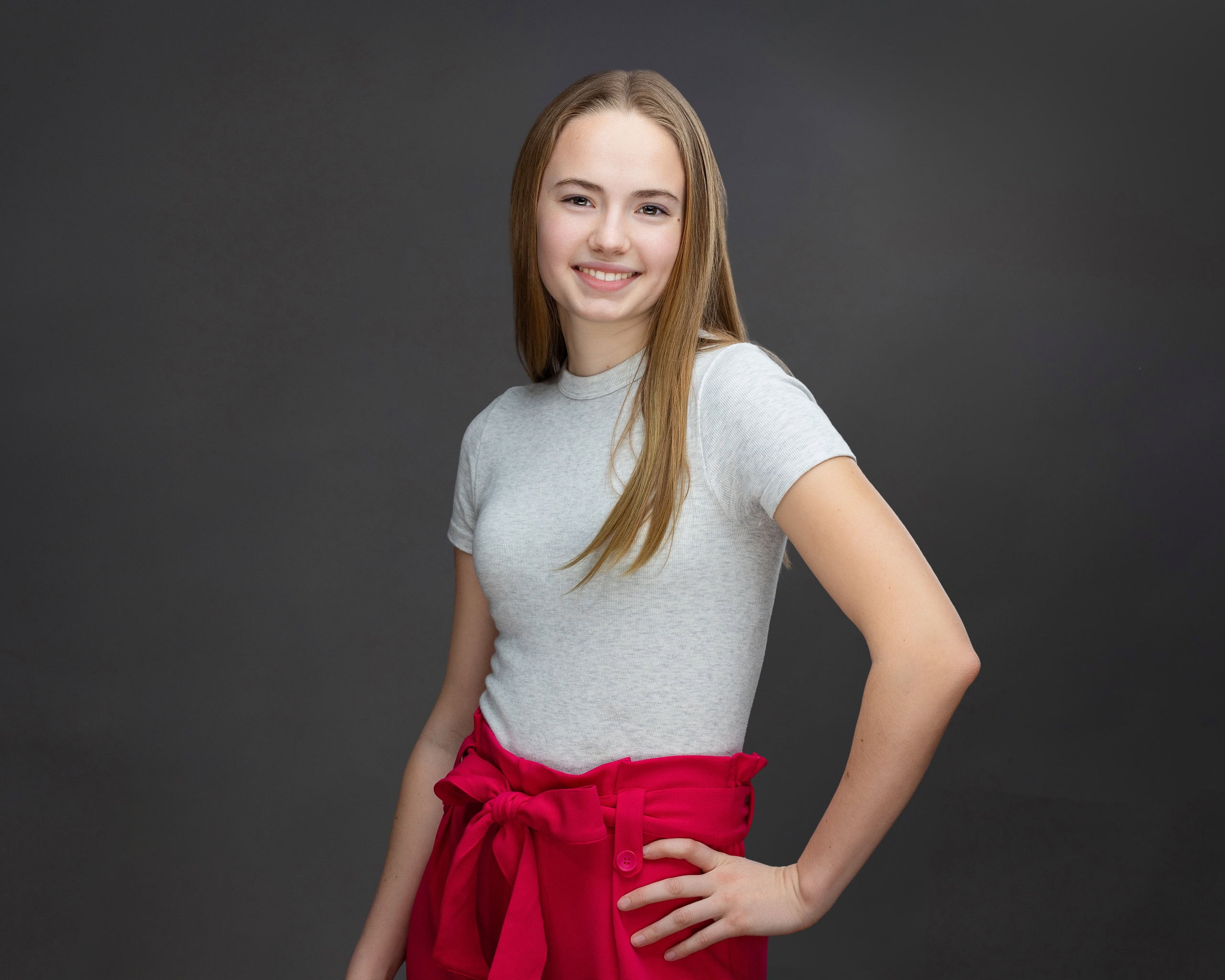 Professional studio headshot of a massage therapist. The young woman has long brown hair and is smiling at the viewer.
