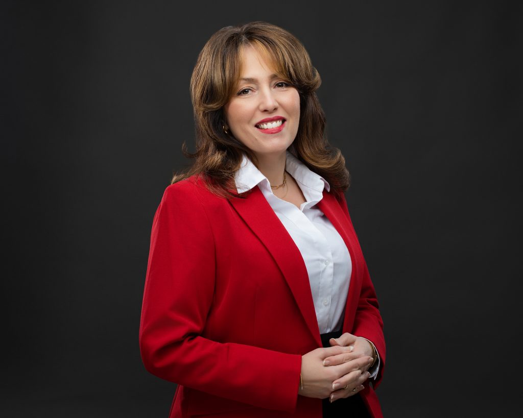 Headshot of a financial consultant. The woman is wearing a red suit jacket against a dark background. She's smiling confidently. 