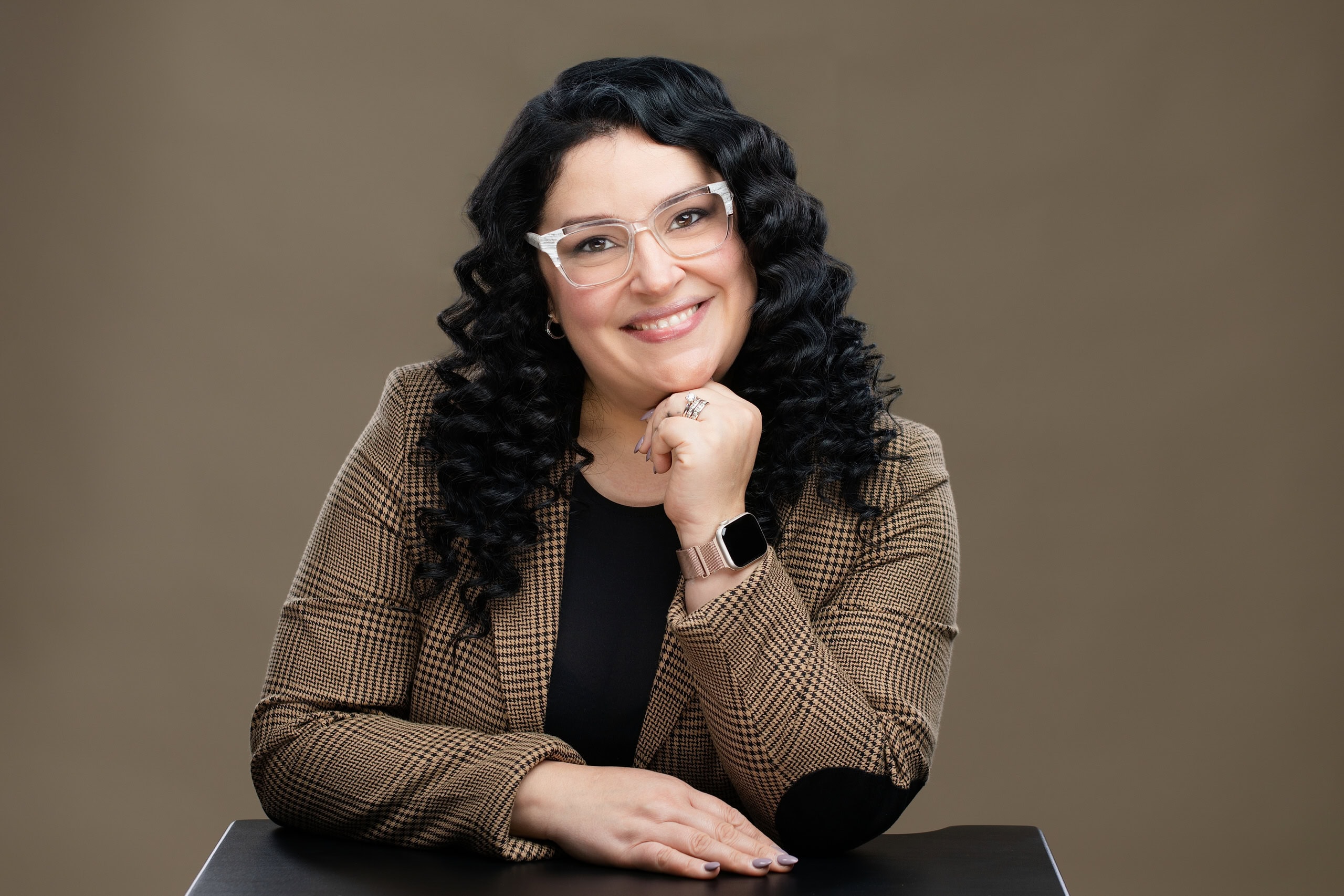 Professional woman's headshot, of a Latina woman resting her chin on her hand and smiling at the viewer.