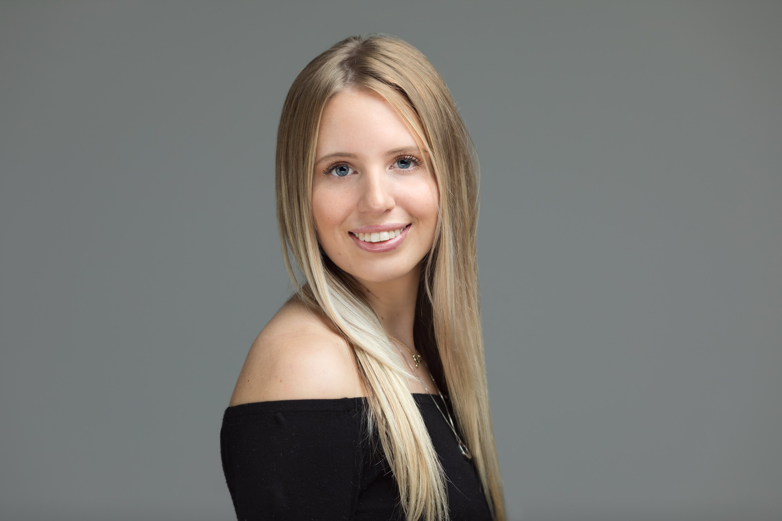 Senior photo of a smiling blond high school senior girl on a light grey studio background.